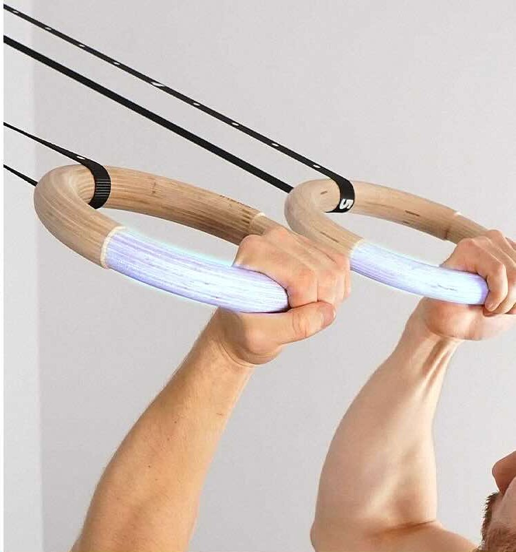 Two hands gripping the lower arcs of a pair of wooden gymnastic rings during a hanging movement, with the gripped sections highlighted