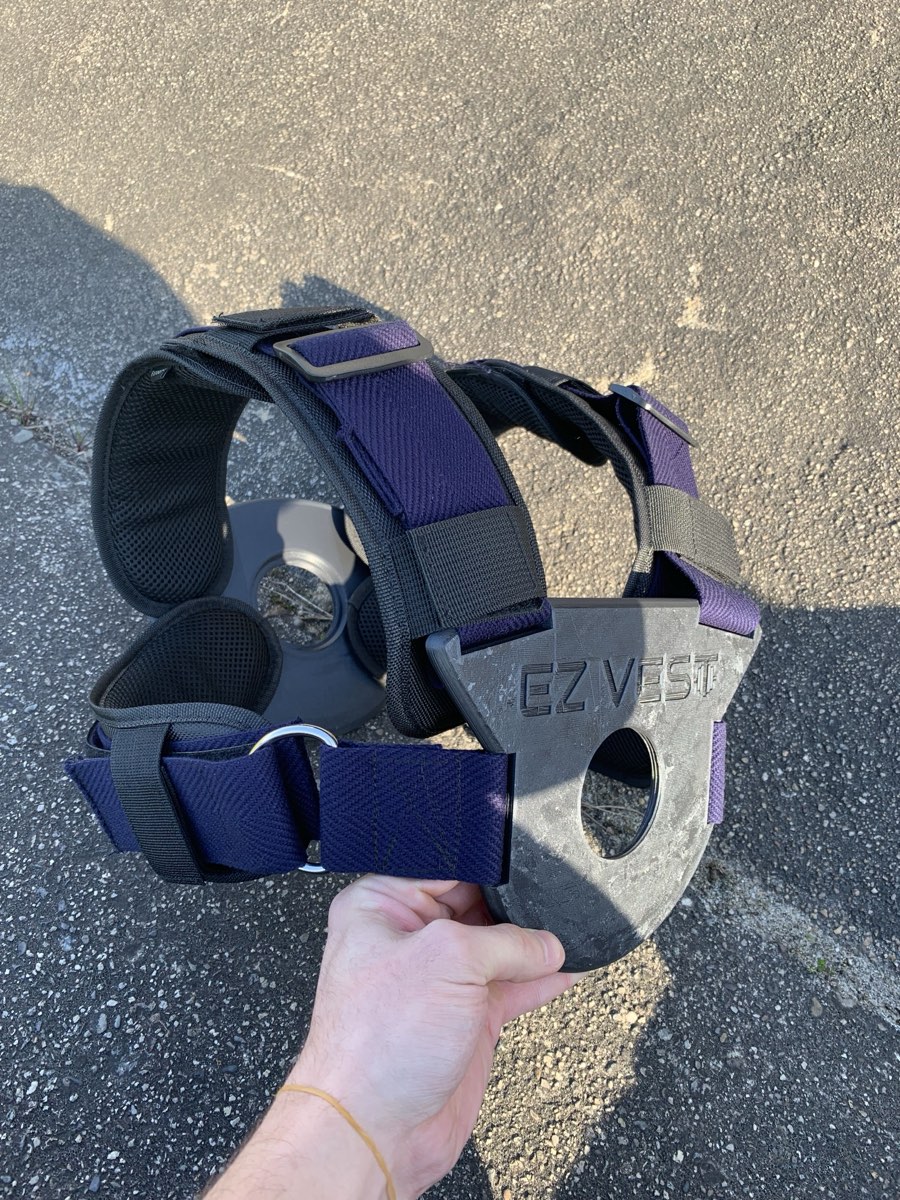 An early weight vest prototype with navy webbing straps and a black 3D printed chest plate, held up in one hand