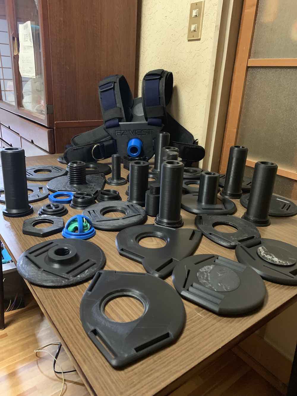 Dozens of black 3D printed weight vest prototypes and loading posts laid out on a wooden table