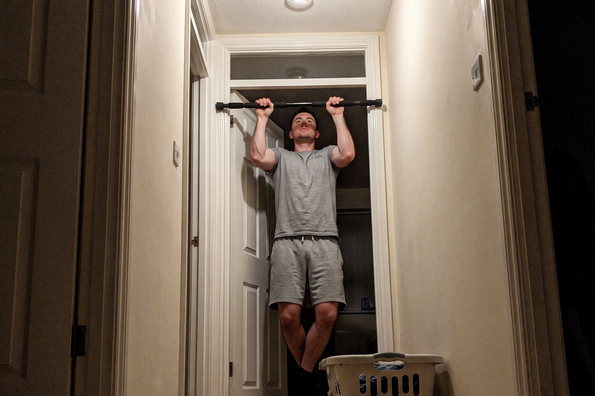 A man at the top of a pull-up on a bar wedged in a doorway of an upstairs hallway