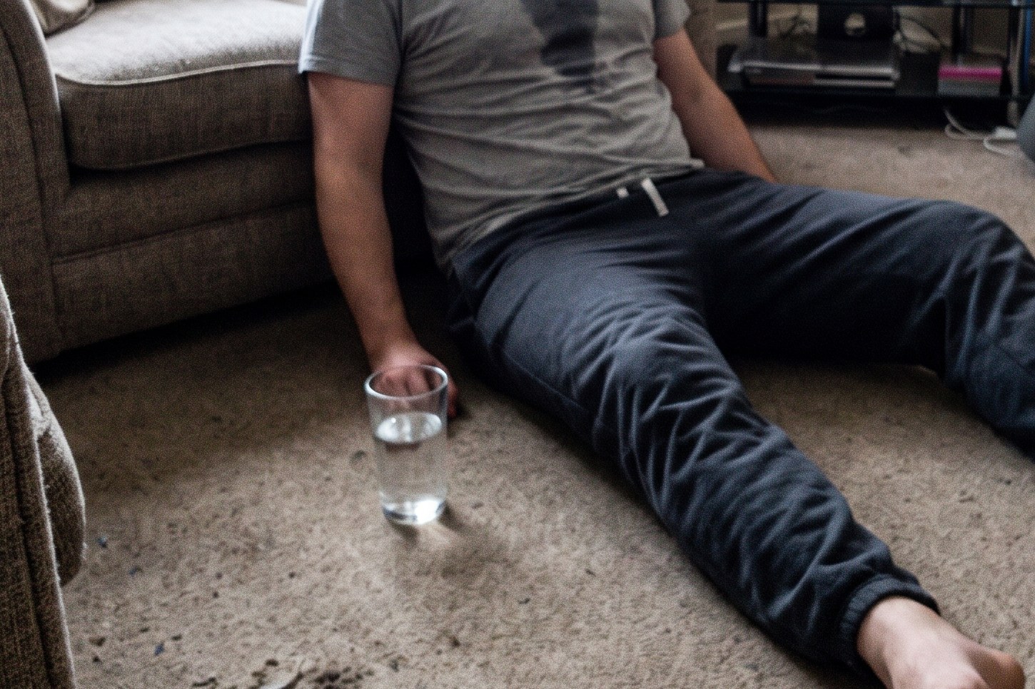 A man sitting on the floor against a sofa after a set, out of breath, a glass of water beside him
