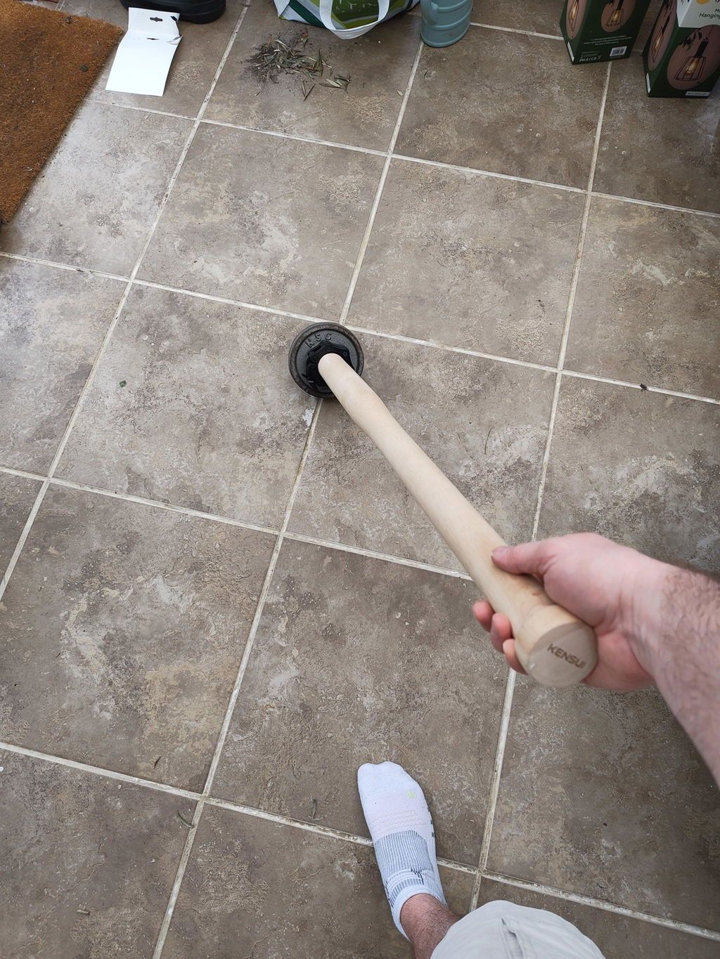 A buyer's phone photo looking down the wooden EZ-MACE PRO handle at the plate on the end, on a tiled floor