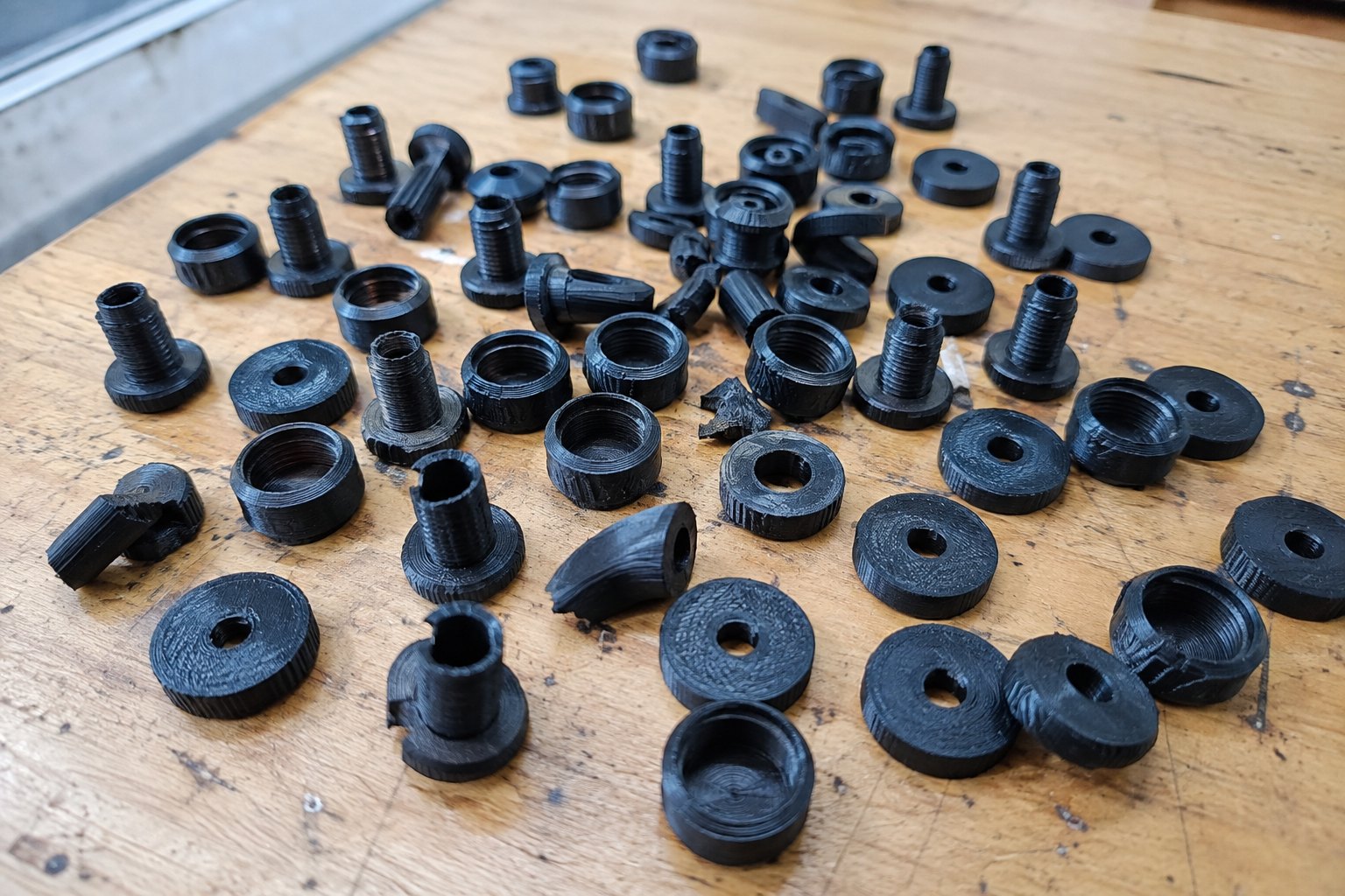 A pile of failed 3D-printed prototype parts from the Kensui workshop, most of them rejected versions of a threaded dumbbell handle.