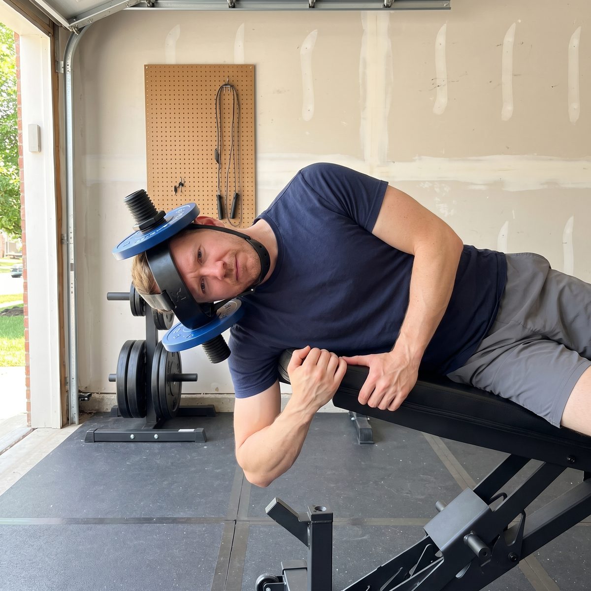 The writer in his garage lying on his side on a bench, doing a side neck raise with a plate loaded helmet