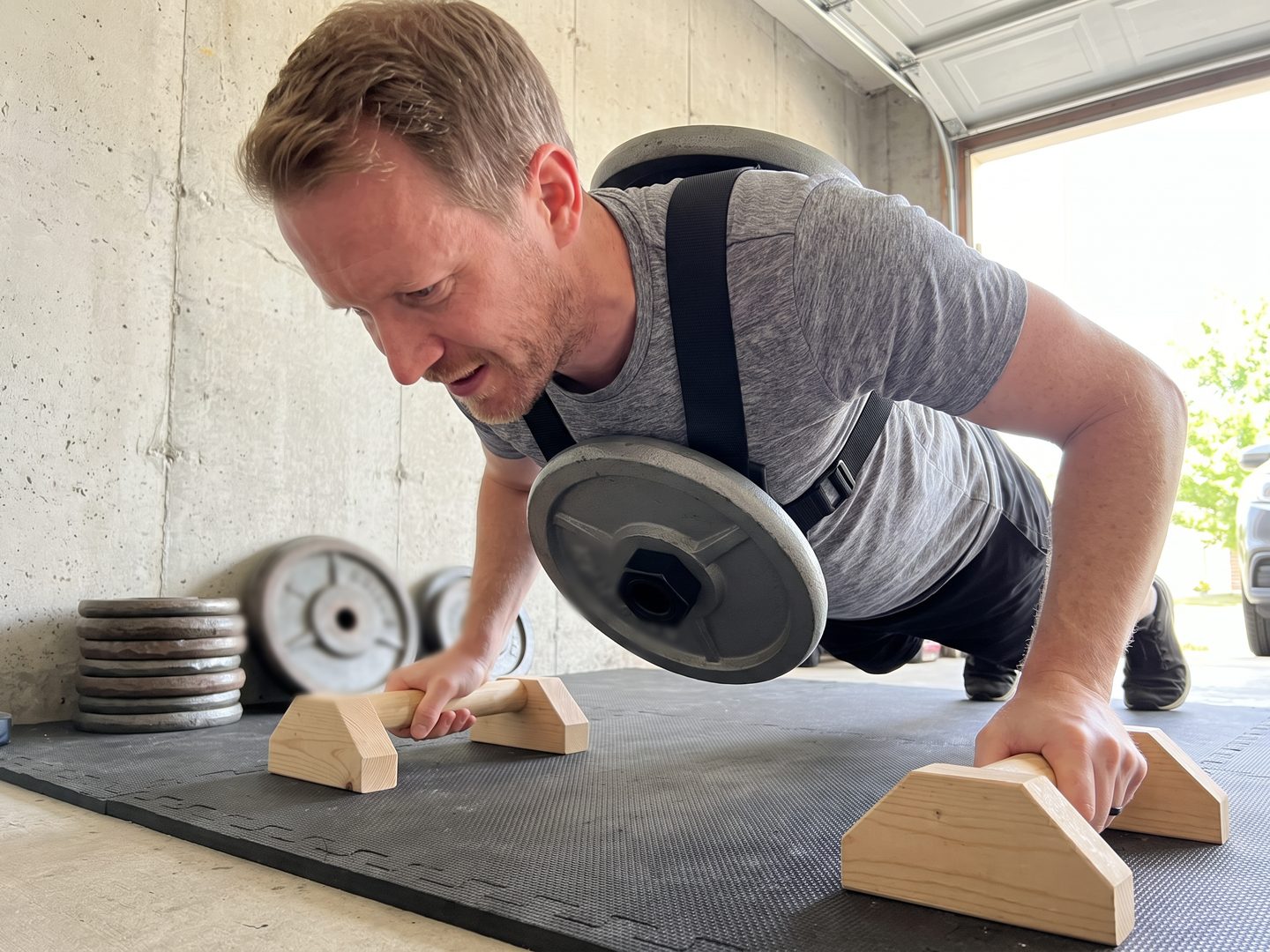 The writer doing a weighted push-up on low wooden parallettes with an iron plate on the chest post clearing the floor