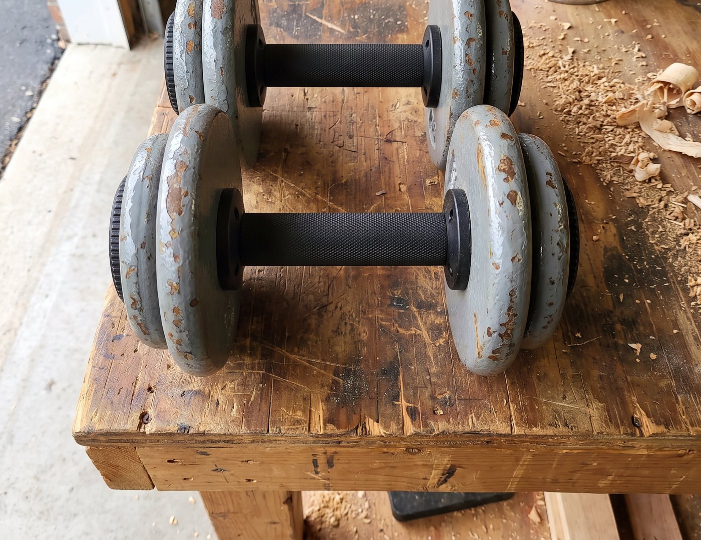 Two black plate loaded dumbbell handles loaded with old grey iron plates on a garage workbench