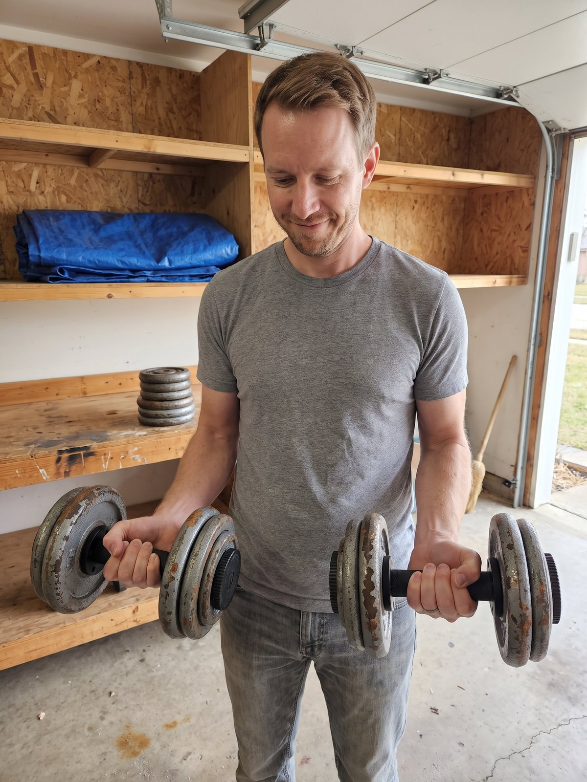 The writer in his father's garage holding a pair of black plate loaded dumbbell handles loaded with old grey iron plates