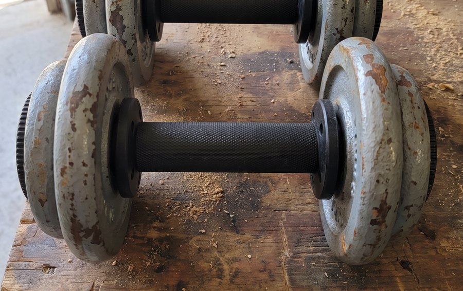 A black plate loaded dumbbell handle loaded with old grey iron plates on a garage workbench