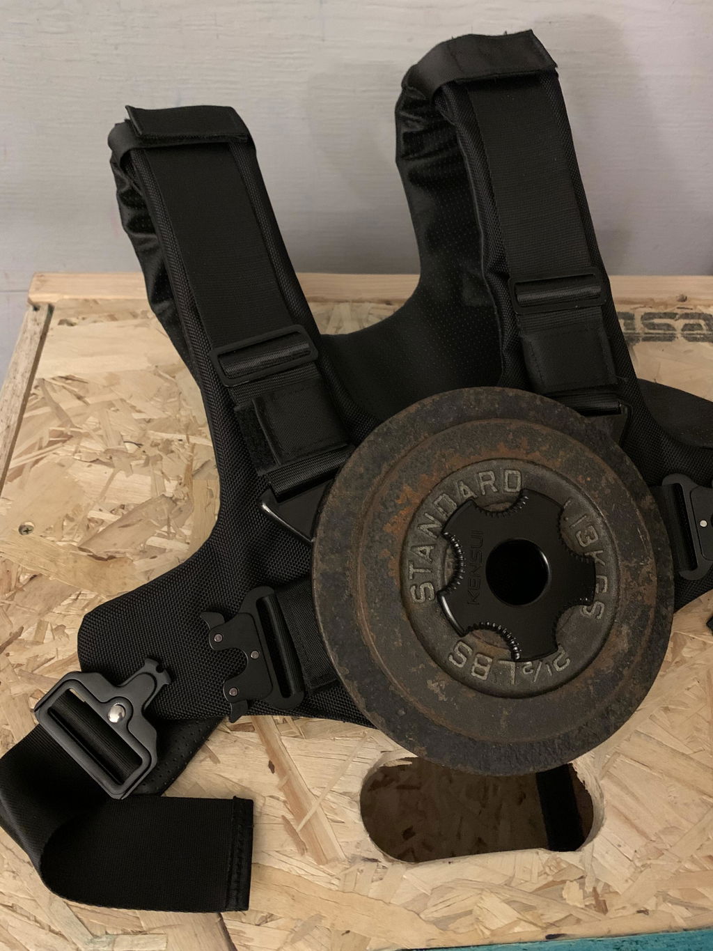 Weight vest with a single plate mounted, resting on a plywood floor