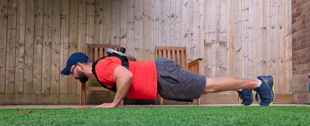 An owner doing a push-up in his garden wearing the loaded vest