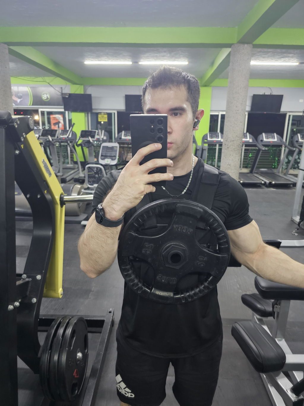A man in a commercial gym wearing a Kensui EZ-VEST with a black iron plate on the chest post
