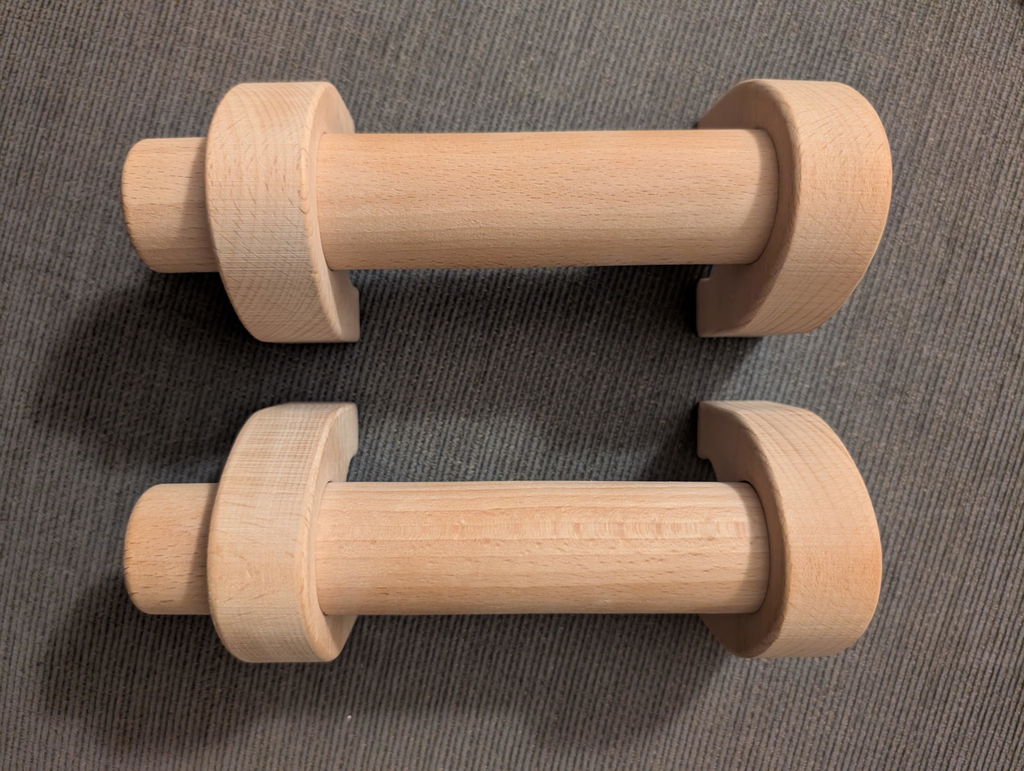 A pair of wooden parallettes lying on a grey carpet, seen from above