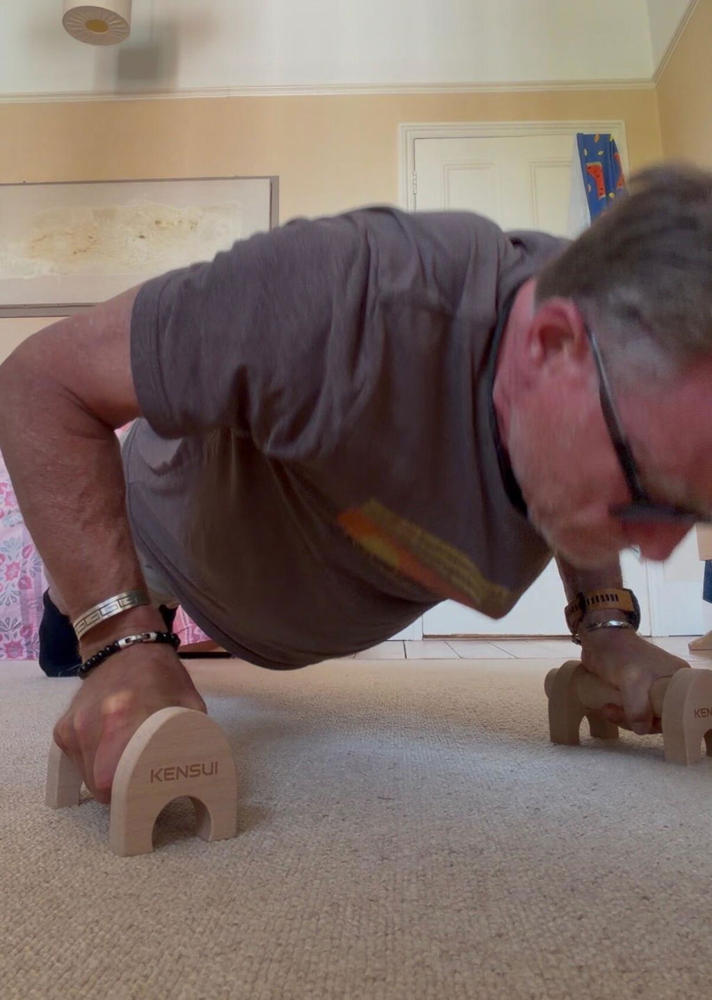 A man doing a push-up on a pair of wooden parallettes on a carpet at home