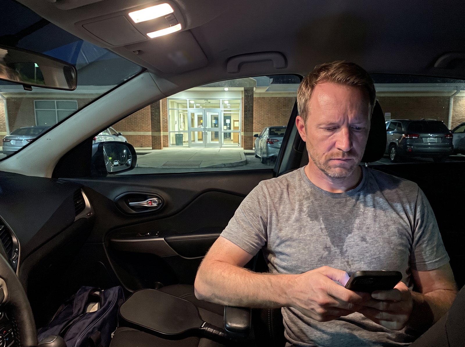 The author in his parked car outside the rec center at night, reading on his phone, paddle and bag on the passenger seat