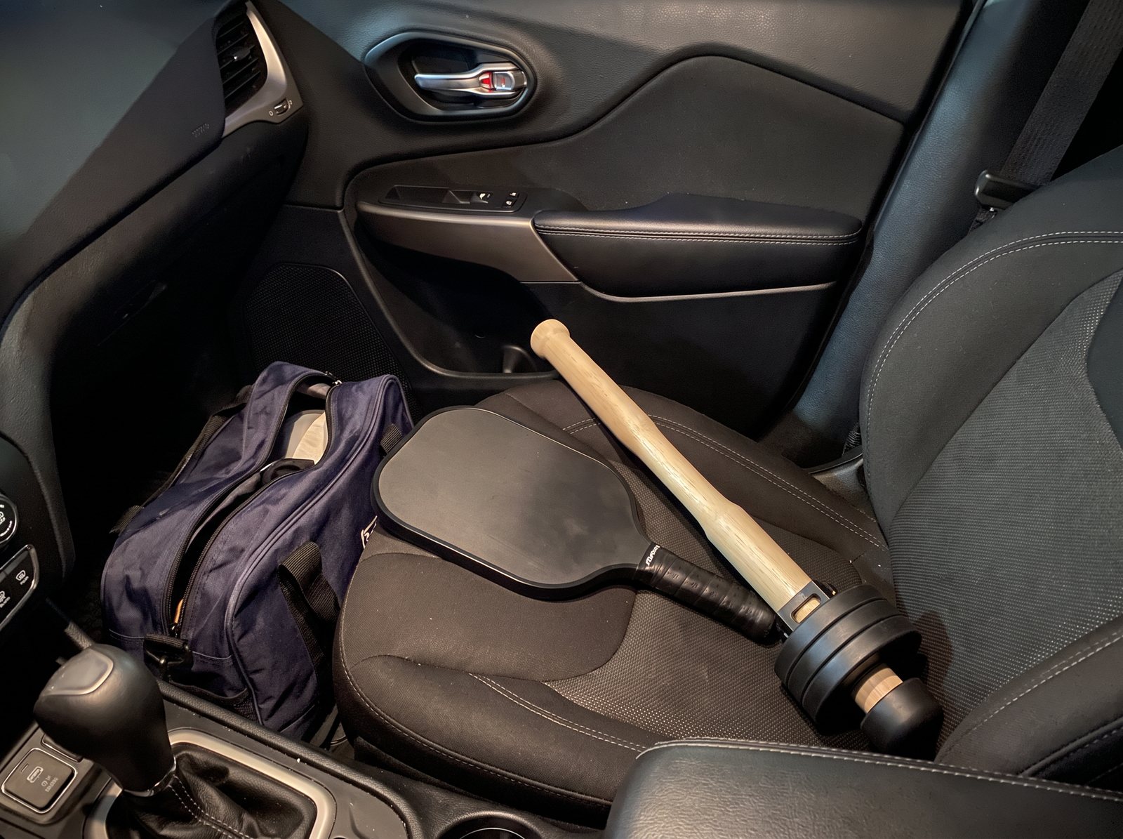 The wooden EZ-CLUB PRO lying on the passenger seat of the author's car beside his court bag and paddle