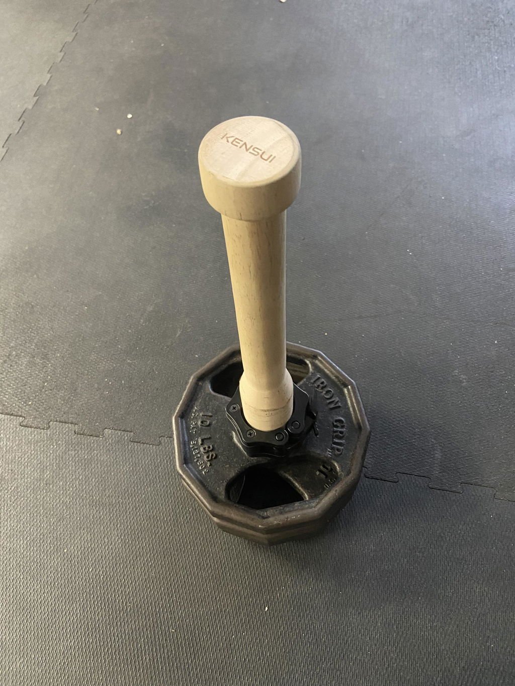 A buyer's phone photo of the wooden EZ-CLUB PRO standing in an iron plate on a gym floor