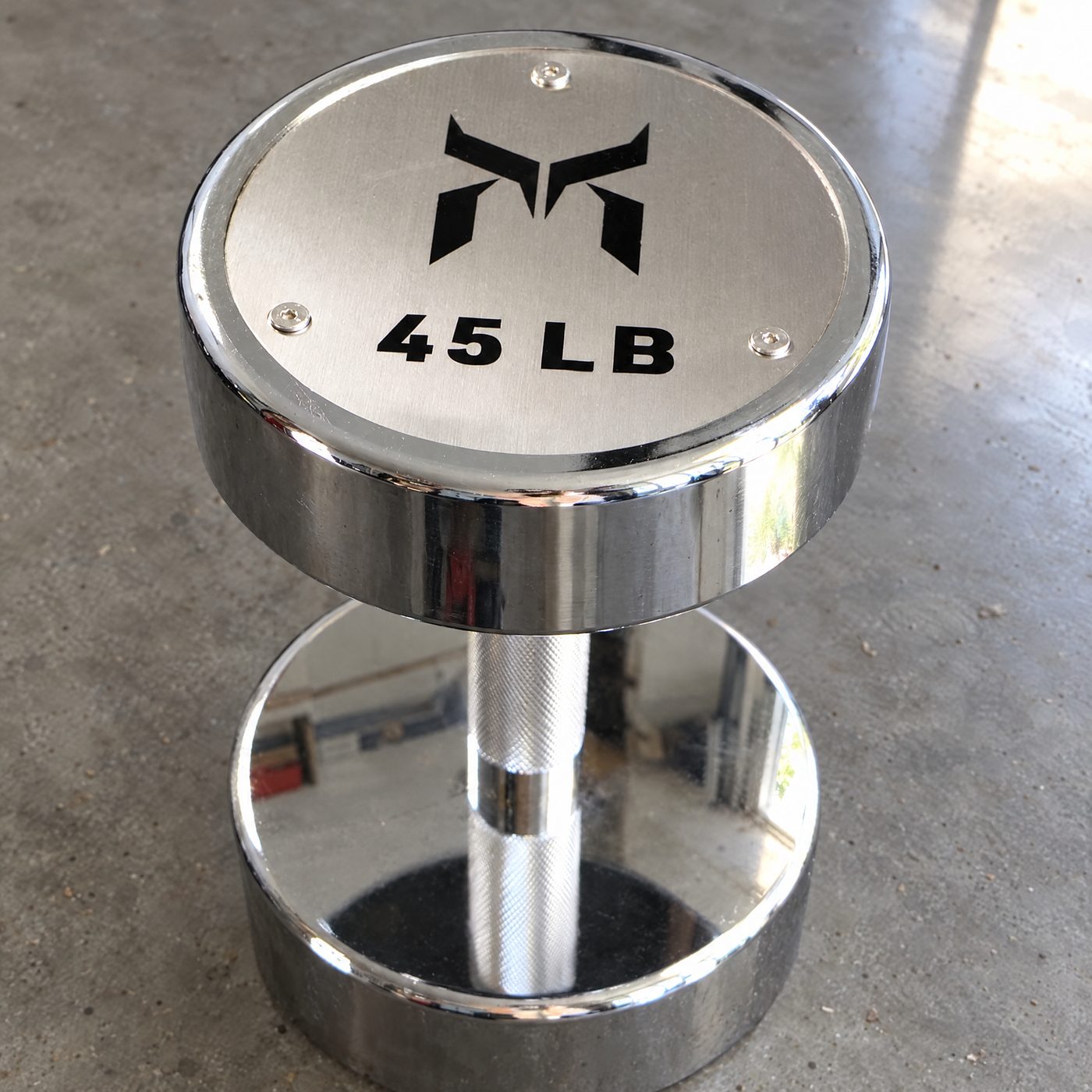 Close up of a chrome 45 pound dumbbell end with the weight and logo on a brushed metal plate, on a concrete floor