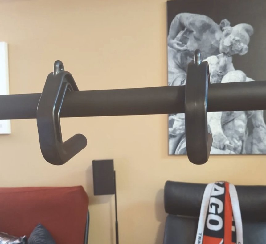 An owner photograph of a wide wall mounted pull-up bar in a home gym with two hooked handles hanging from it