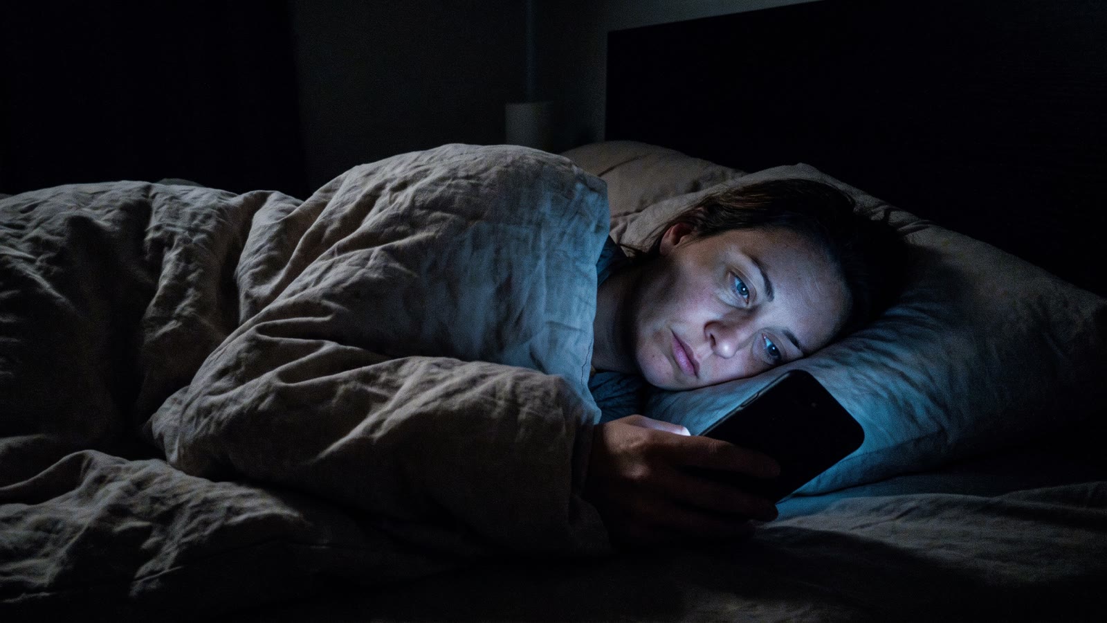 A woman lying awake in bed at night lit by her phone screen